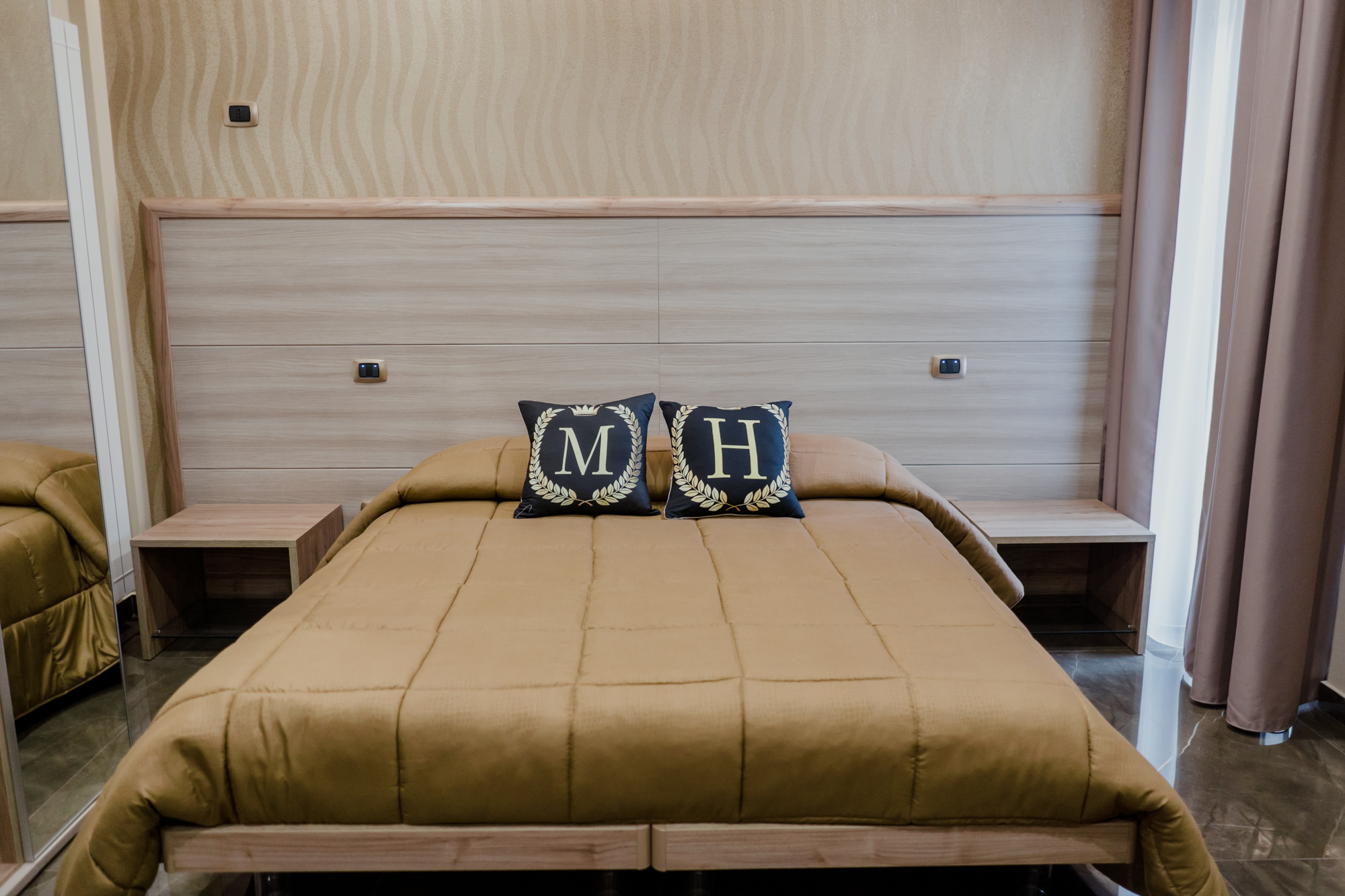 Letto matrimoniale della Camera Quadrupla 1 di Miryam House con cuscini MH e testata in legno chiaro